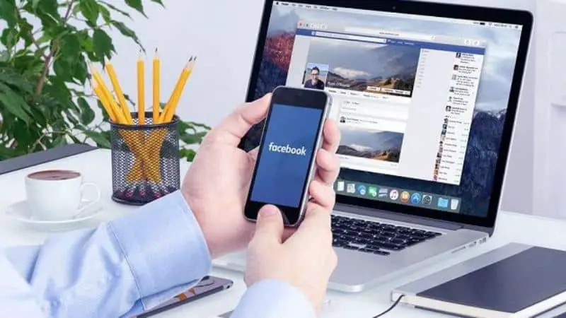 laptop con facebook e mani sul cellulare con matite e taccuino di facebook