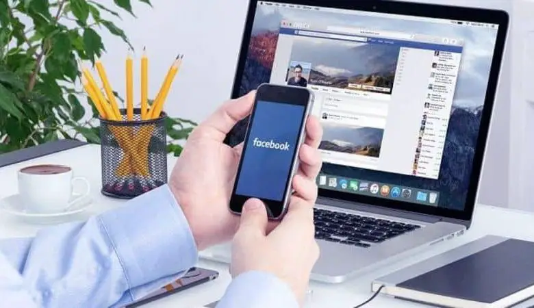 laptop con facebook e mani sul cellulare con matite e taccuino di facebook