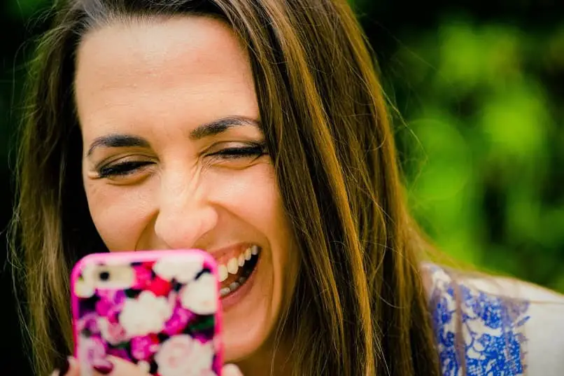 donna dai capelli castano scuro che guarda il suo cellulare sorride felice cambiando le immagini dei suoi social network come font nei post di Instagram